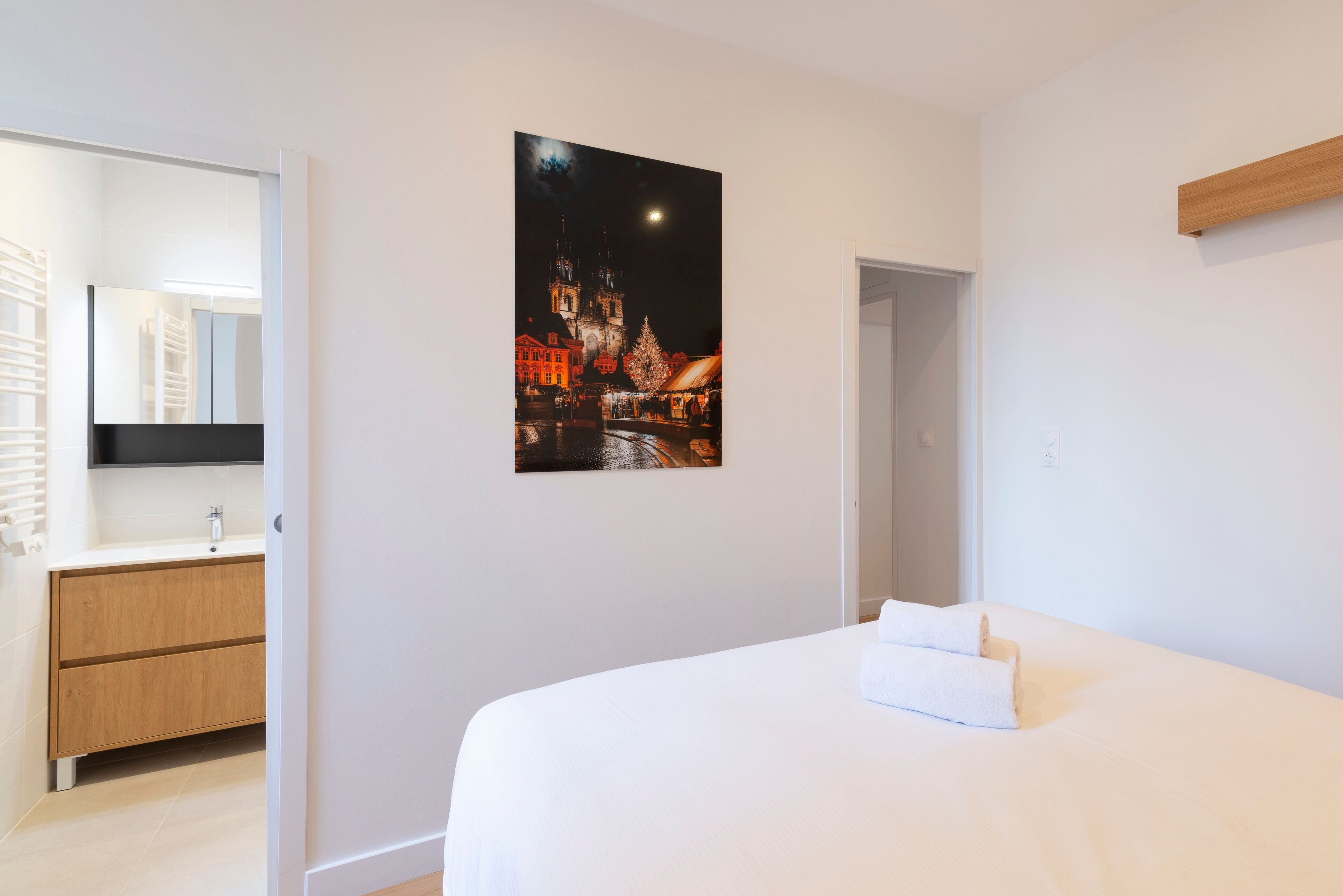 Ein Hotelzimmer mit einem Bett, einem Holzschrank, einem Spiegel und einem gerahmten Bild einer belebten Stadt bei Nacht.