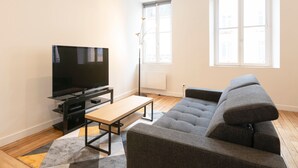 A modern living room with a flat-screen TV, a grey sofa, a wooden coffee table, and a floor lamp.