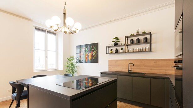 A modern kitchen with a central island, dark cabinetry, a wooden backsplash, and a pendant light.