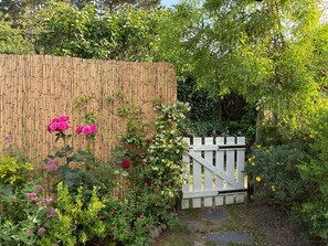Een tuin met een bamboebeschoeijing, bloeiende planten en een wit hek.