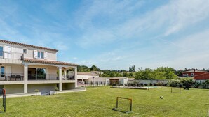 Un edificio de dos pisos con balcón, patio cercado y un arco de fútbol.