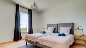 Un dormitorio con una cama grande, dos almohadas, una mesita de noche con una lámpara y vistas al exterior.