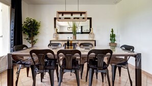 Un comedor con una amplia mesa rectangular, seis sillas, una lámpara central y dos plantas en macetas.