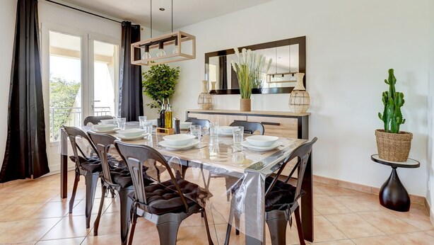 Un comedor con una mesa dispuesta para cuatro, sillas, un florero y una planta de cactus.