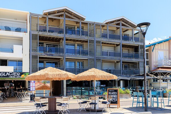 A multi-story hotel with outdoor seating and umbrellas, balconies, and a visible sign for Glacier Beach Coffee. - MimiZen - Vue sur l'océan, la plage de la Garluche (Mimizan)