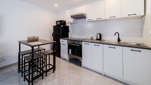 A modern kitchen with white cabinets, a black refrigerator, a built-in oven, and a sink. There is a small dining area with a table and stools. - Batié - Appt 4 personnes à Mulhouse (Mulhouse)