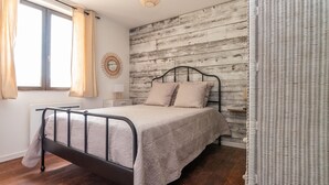 A bedroom with a metal bed frame, a wooden headboard, a bedside table with a lamp, and a window with curtains. - L'appartement de Marie - Appt avec terrasse (Chalon-sur-Saone)