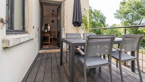 An outdoor balcony with a table and chairs, a covered umbrella, and a view of the greenery. - L'appartement de Marie - Appt avec terrasse (Chalon-sur-Saone)
