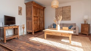 A living room with a wooden floor, a sofa, a coffee table, a TV, and a cabinet. - L'appartement de Marie - Appt avec terrasse (Chalon-sur-Saone)