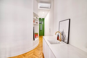 A narrow hallway with a white sink and a framed picture on the wall, leading to a green door.