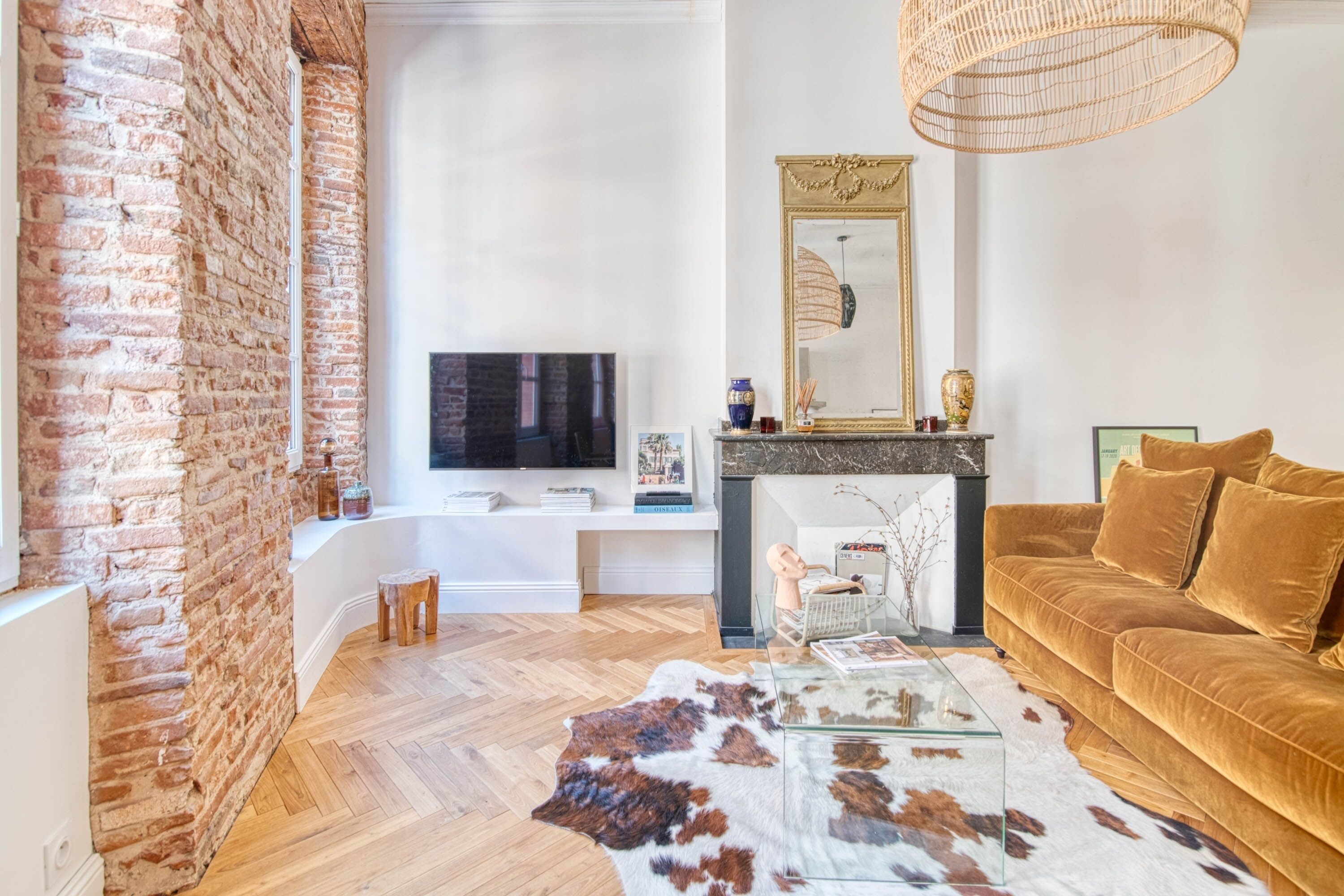 A modern living room with a brick wall, a flat-screen TV, a fireplace, a sofa, and a cowhide rug.