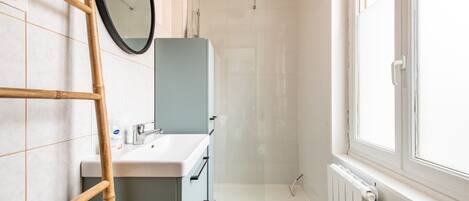 A bathroom with a shower, a sink, and a window.