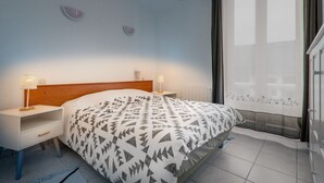 A bedroom with a bed, two bedside tables, a nightstand, a window with curtains, and a ceiling light.