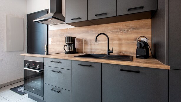 A modern kitchen with dark cabinetry, a wooden countertop, a built-in oven, and a coffee maker.
