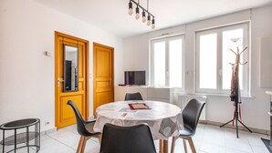 A dining area with a round table, four chairs, a television, and a coat rack.