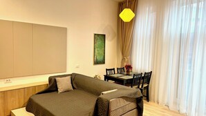 A modern bedroom with a bed, a dining table with chairs, a yellow pendant light, and sheer curtains. - NIce Flat in Villa Near Old Town
 (București)