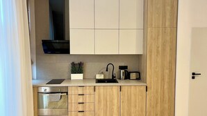 A compact kitchen with a built-in oven, a microwave, a sink, and wooden cabinetry. - NIce Flat in Villa Near Old Town
 (București)
