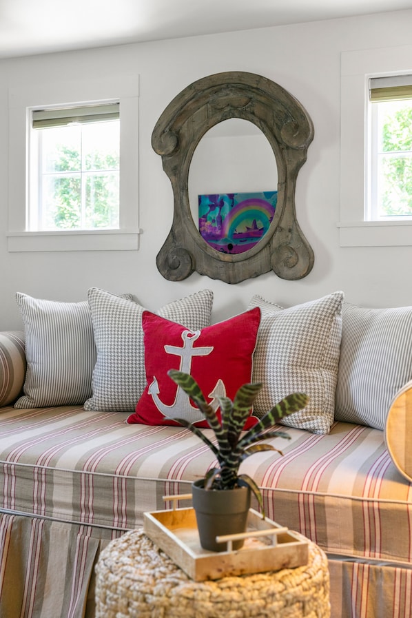 Una sala de estar acogedora con un sofá a rayas, un espejo decorativo y una planta en maceta.