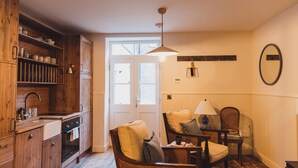 A cozy kitchen with wooden cabinets, a sink, and a dining area with wicker chairs and a table. - Rockpool Cottage 5 Buckingham Mews Coastal Retreat (Broadstairs)