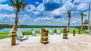 Un espace de détente aménagé au bord de la plage, avec des chaises longues et des poteaux en bois, offrant une vue sur un lac paisible et une côte lointaine.