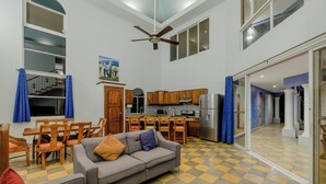 Amplia sala de estar con sofá, mesa de comedor y sillas, cocina con armarios de madera y suelo a cuadros.
