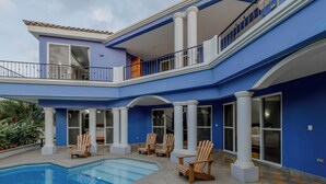 Edificio de dos pisos con piscina, mobiliario exterior y amplias ventanas.