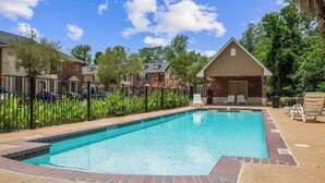A rectangular swimming pool with a brick border, surrounded by a fence and lounge chairs.