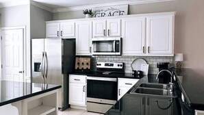 A modern kitchen with white cabinetry, stainless steel appliances, and a black countertop.