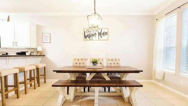 A dining area with a wooden table and bench, a hanging light fixture, and a wall sign that reads "this is the happy place".