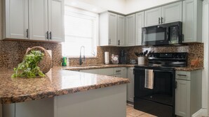 Una cocina con encimeras de granito, estufa negra, microondas y armarios verde claro.