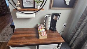 Een houten tafel met een koffiezetapparaat, een dienblad met koffiekapsules en een lijst met een koffiequote aan de muur.