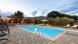 A swimming pool with lounge chairs and a pergola with lights, surrounded by stone tiles and greenery. - Villa Castiglione 9, Emma Villas (Castiglione della Pescaia)