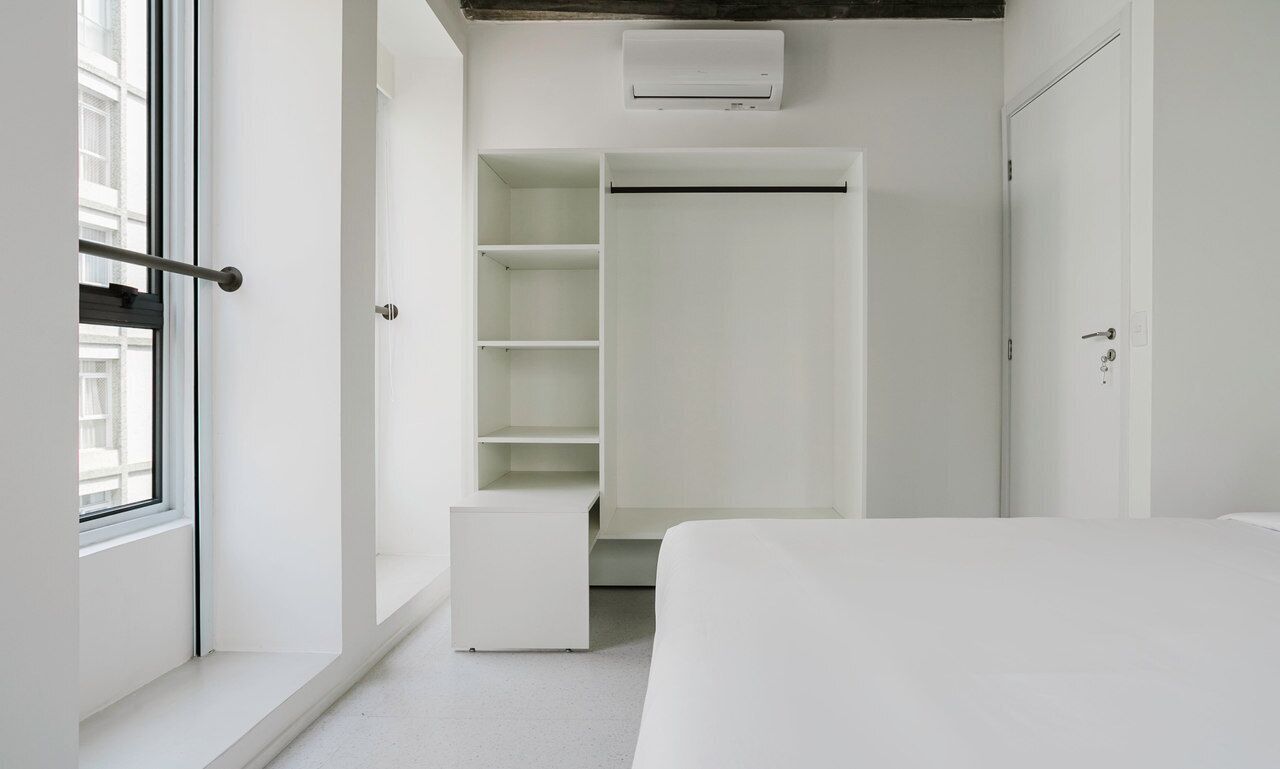 A minimalist bedroom with a large bed, a walk-in closet, and a window providing natural light.