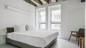 Ein modernes Schlafzimmer mit einem großen Bett, einem Sessel und großen Fenstern.