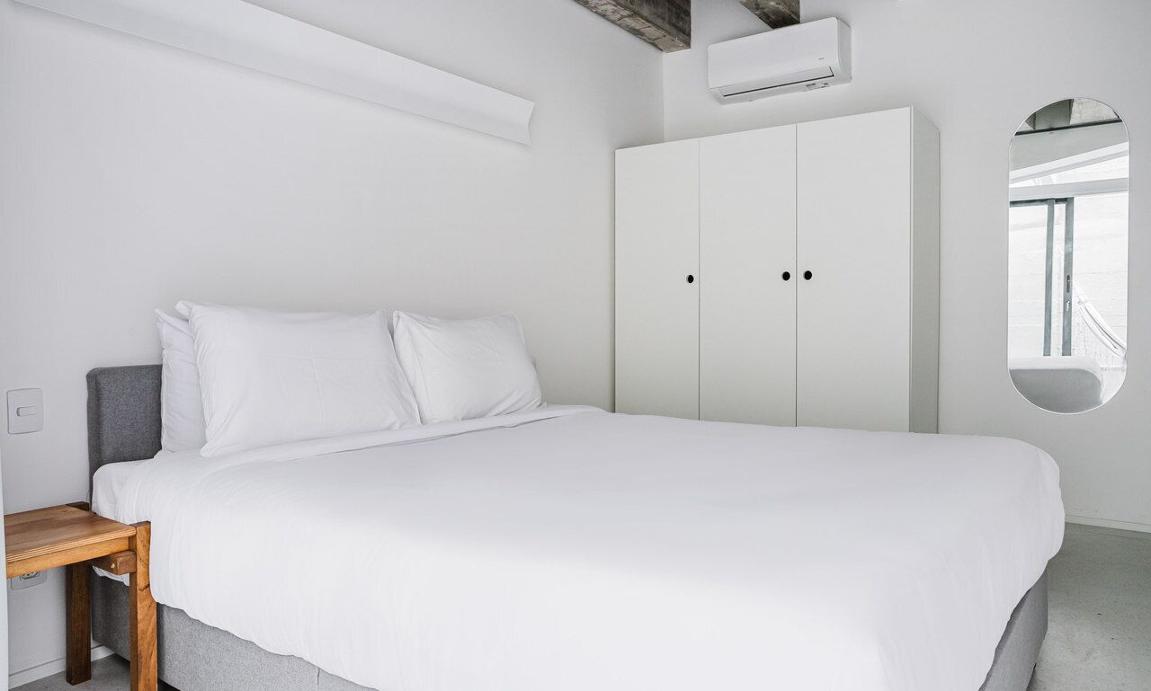Un dormitorio con una cama grande, una mesita de noche de madera, un armario y un espejo redondo en la pared.