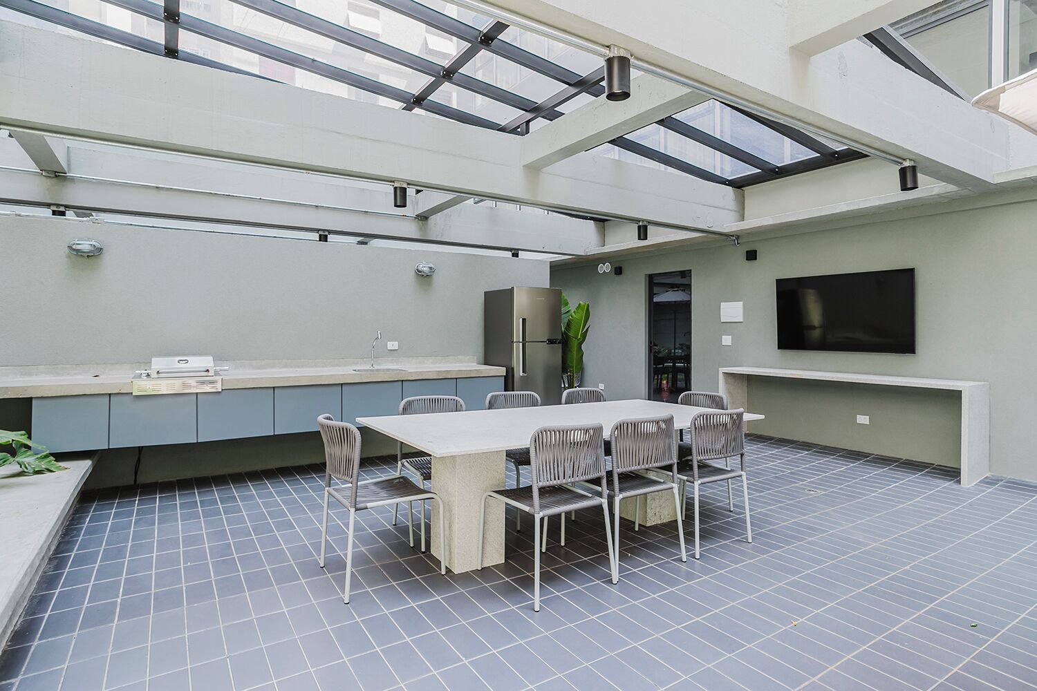 A modern kitchen with a dining area, featuring a large table, chairs, a built-in oven, and a TV mounted on the wall.