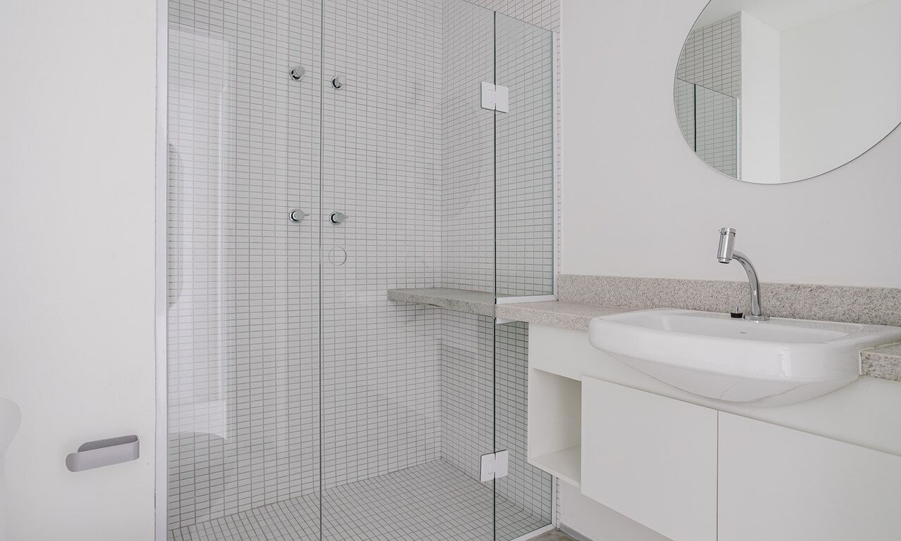 Een moderne badkamer met een douchecabine van glas, een witte wastafel en een ronde spiegel.