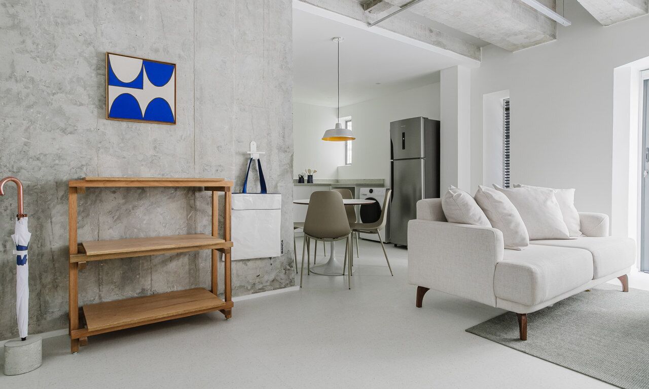 A modern living room with a white sofa, a wooden shelf, and a dining area with chairs.