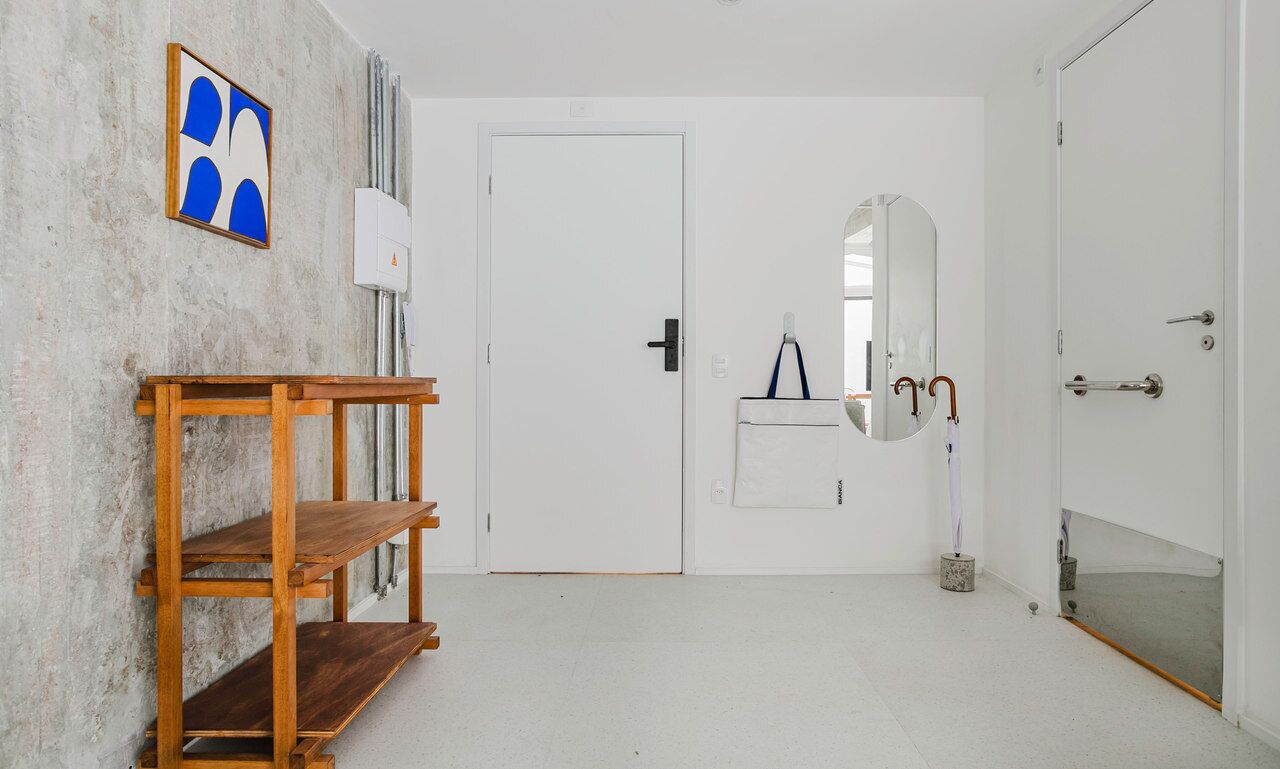 Una habitación con una puerta blanca, una estantería de madera, un espejo y un perchero.