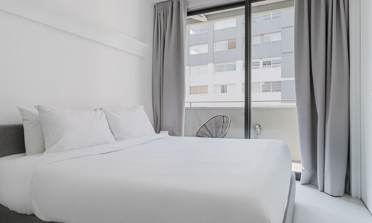 Un hotel moderno con una cama grande, cortinas grises y vistas a un edificio desde la ventana.