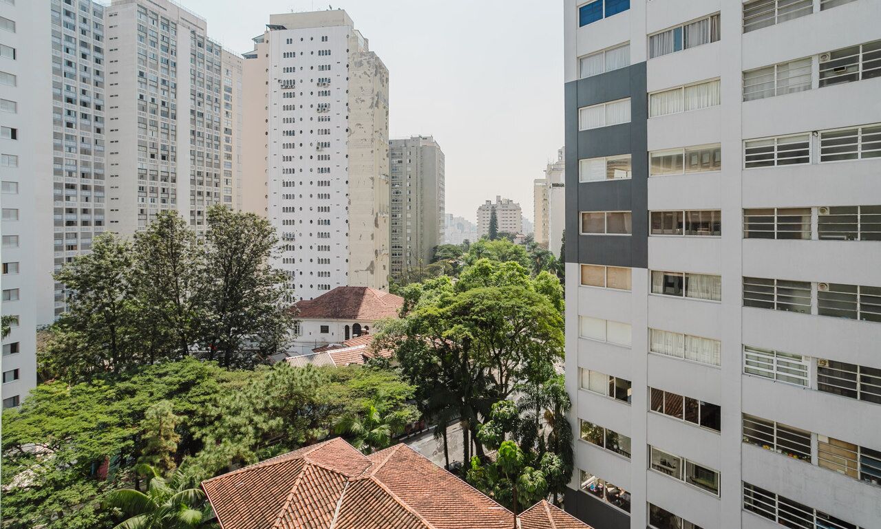 A high-rise building with multiple floors, surrounded by greenery and a smaller building with a red-tiled roof.
