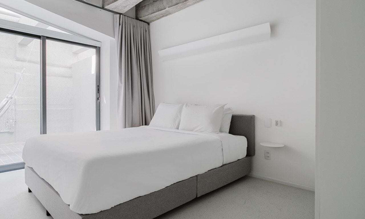 Una camera da letto moderna con un letto grande, una porta scorrevole in vetro su un balcone e un design minimalista.