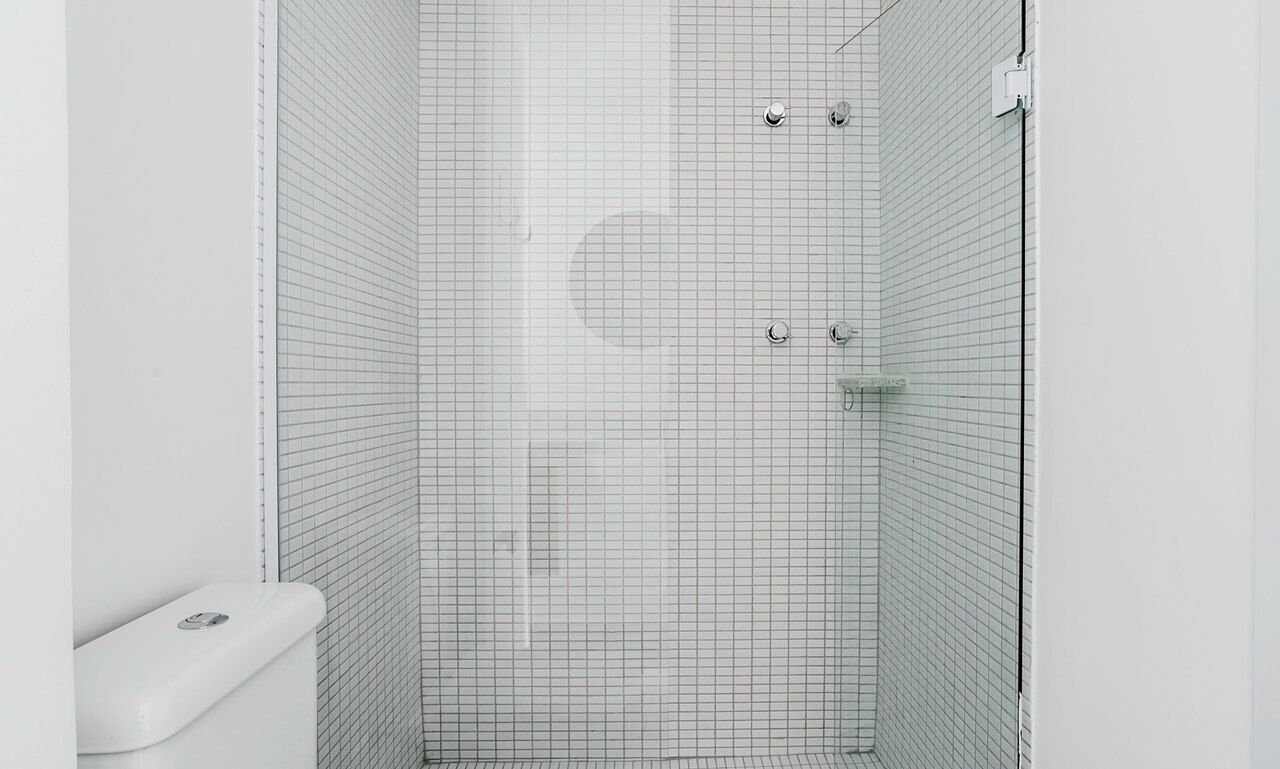 A modern bathroom with a grid-patterned shower wall, a white toilet, and a visible shower control panel.
