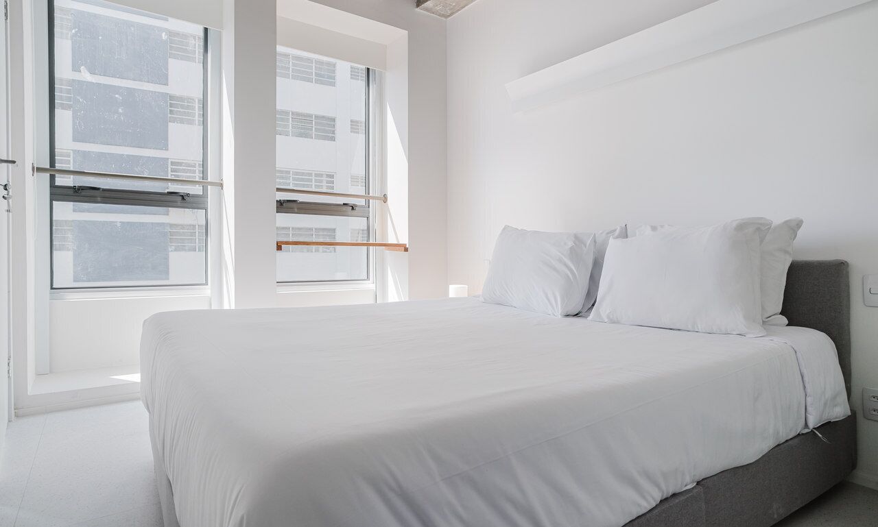 Ein Schlafzimmer mit Bett, weißen Wänden und großen Fenstern.