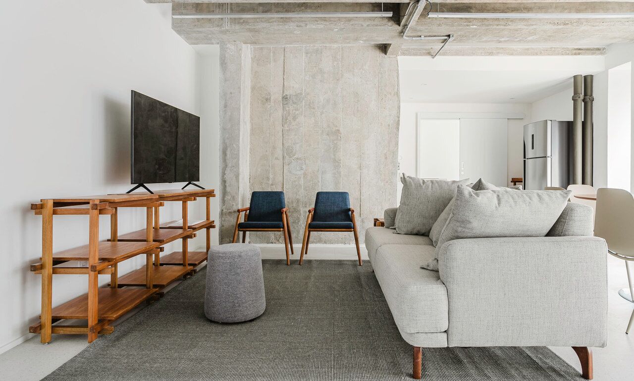 A modern living room with a grey sofa, two blue chairs, a wooden TV stand, and a grey ottoman.