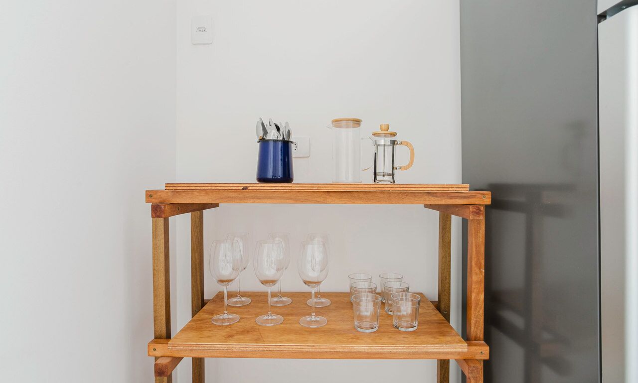 A wooden table with a shelf holding wine glasses and a coffee pot.