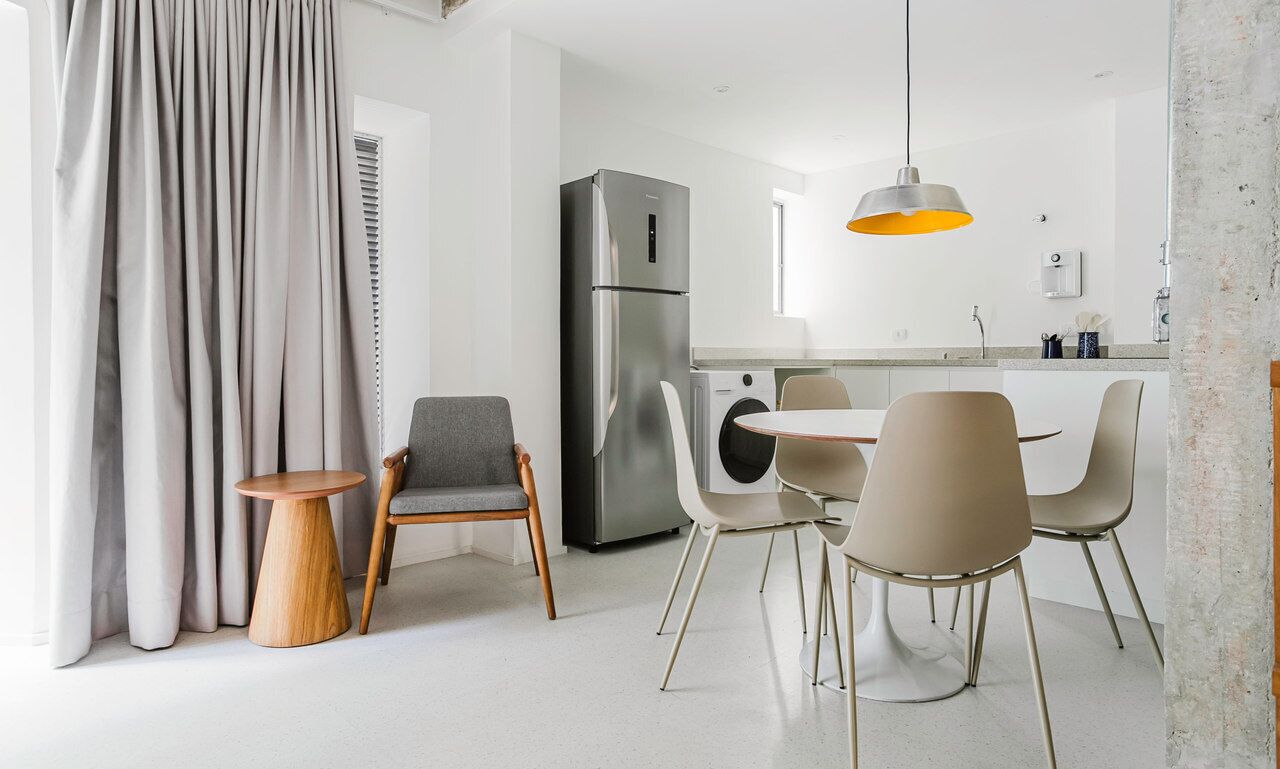A modern kitchen with a stainless steel refrigerator, a dining area with a round table and chairs, and a pendant light above the table.