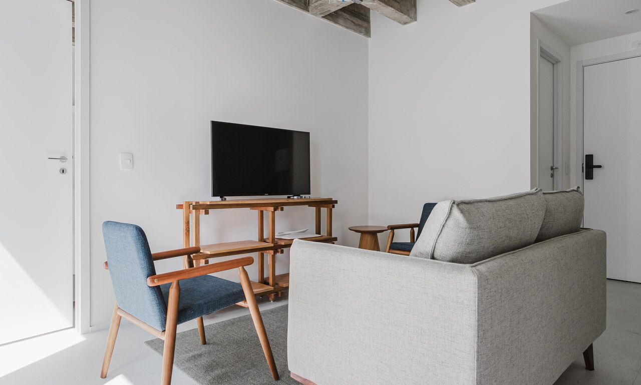 A modern living room with a grey sofa, blue chairs, a wooden coffee table, and a flat-screen TV mounted on the wall.