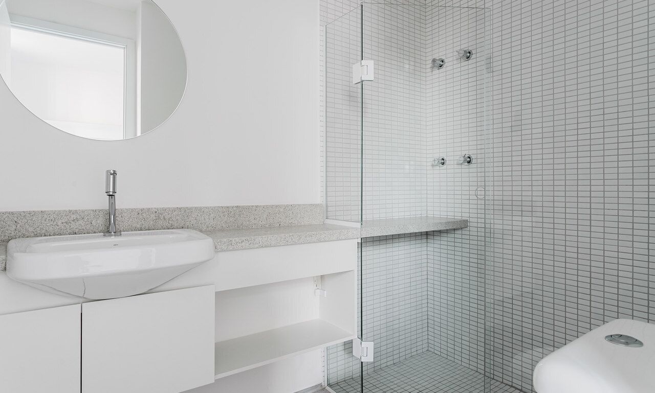 A modern bathroom with a white sink, a round mirror, and a glass-enclosed shower area.