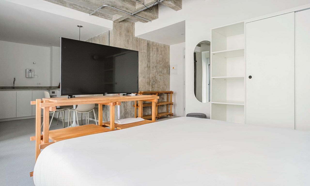 Ein modernes Schlafzimmer mit einem großen Bett, einem Holztisch, einem Flachbildfernseher und einem begehbaren Kleiderschrank.